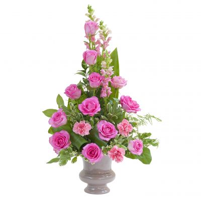pink flowers arranged in a plastic urn in traditional triangular garden style. this type of floral arrangement is popular option to send to visitation or funeral service. 