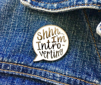 Enamel pin with 'Shh... I'm Introverting' text on a denim background