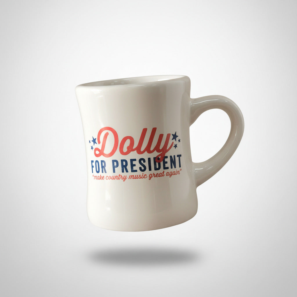 A white ceramic mug with the text 'Dolly FOR PRESIDENT' in red and blue, subheading: make country music great again