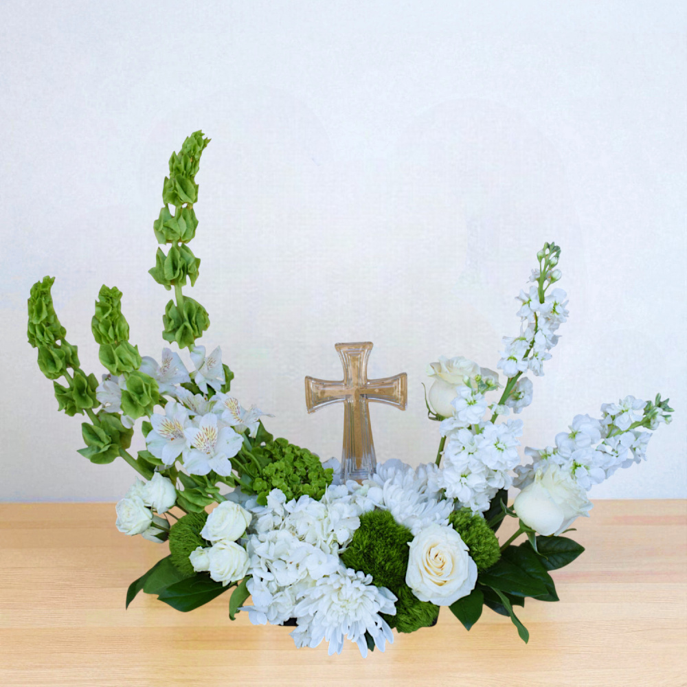 Sacred Farewell is a fuller sympathy arrangement with white and green flowers and a crystal cross. Thoughtfully designed and handcrafted in Houston, TX by Scent and Violet.
